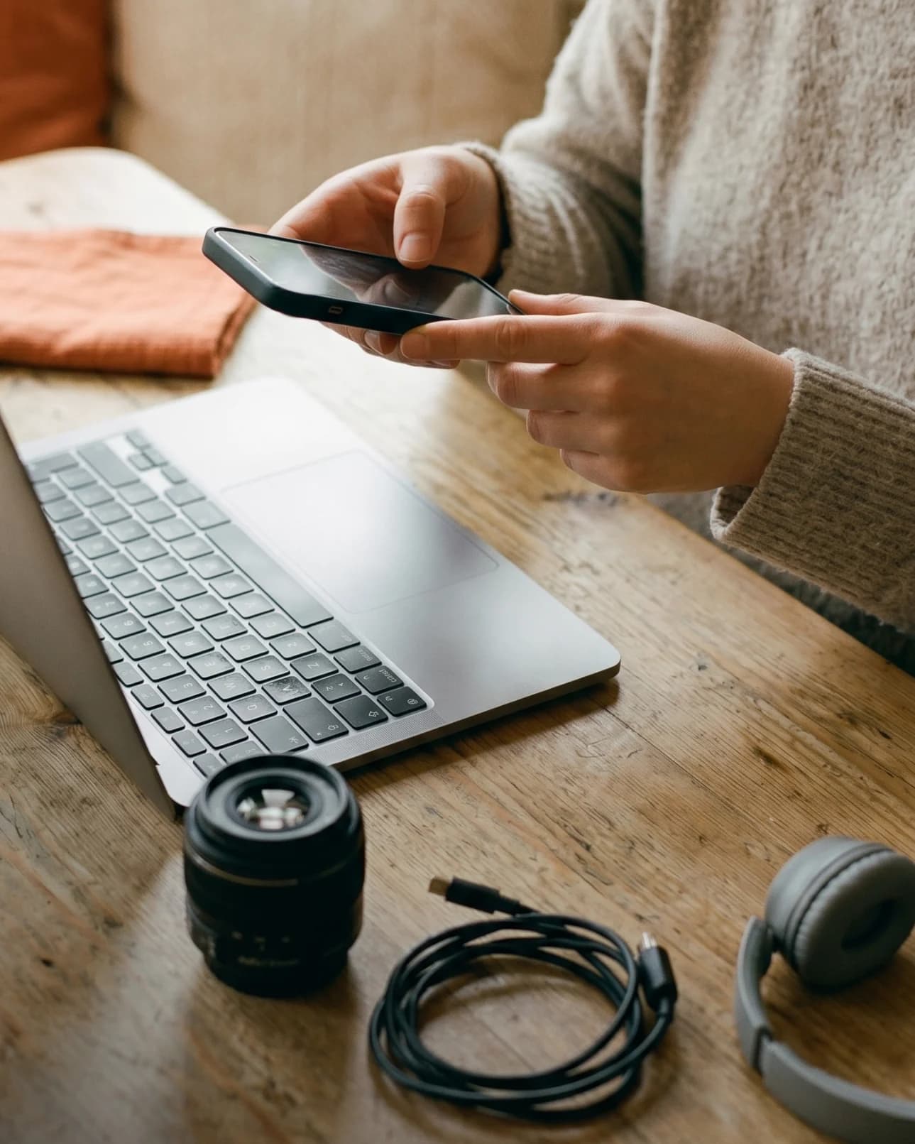 Seller using a phone beside a laptop and accessories while preparing an item description.